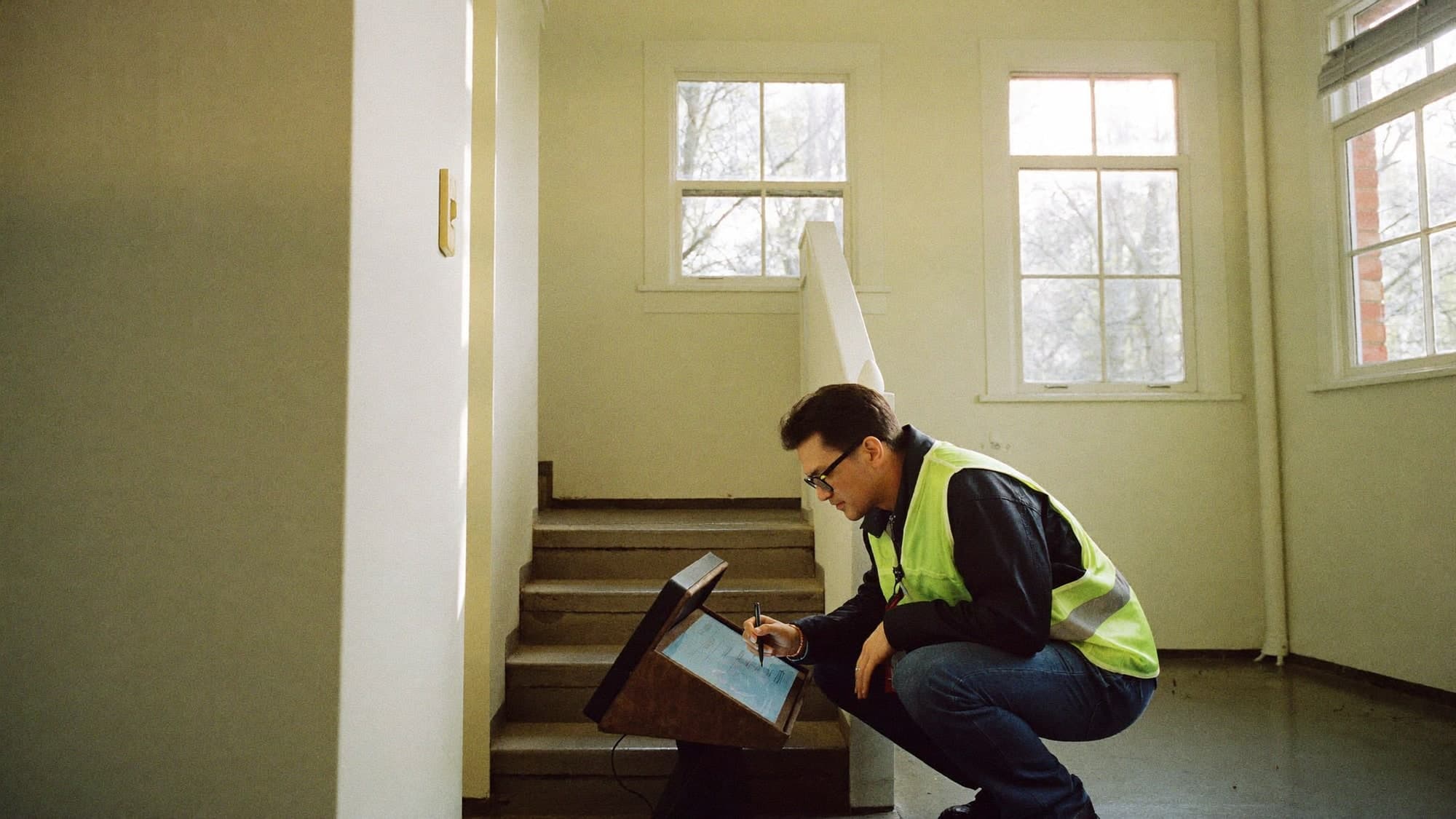 A surveyor recording condition on a tablet in a communal stairwell.