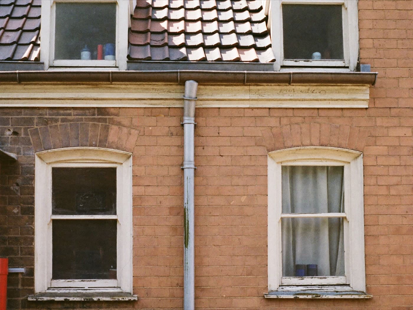 The ageing fabric of a house — sash windows, brickwork, downpipe and roof tiles.